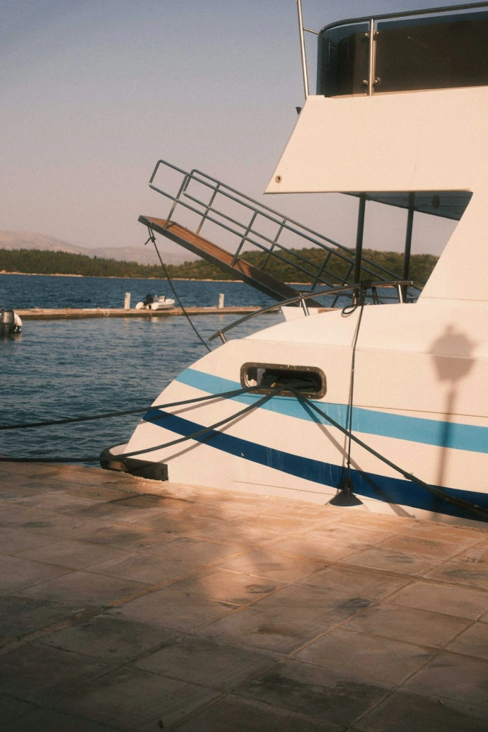 A white yacht with blue stripes moored at a stone pier by the sea.
